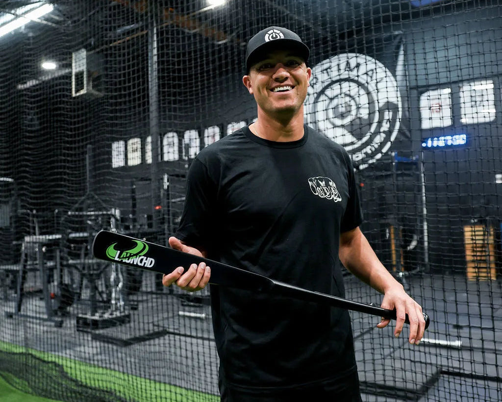 Man holding a baseball bat in an indoor batting cage with a target in the background.